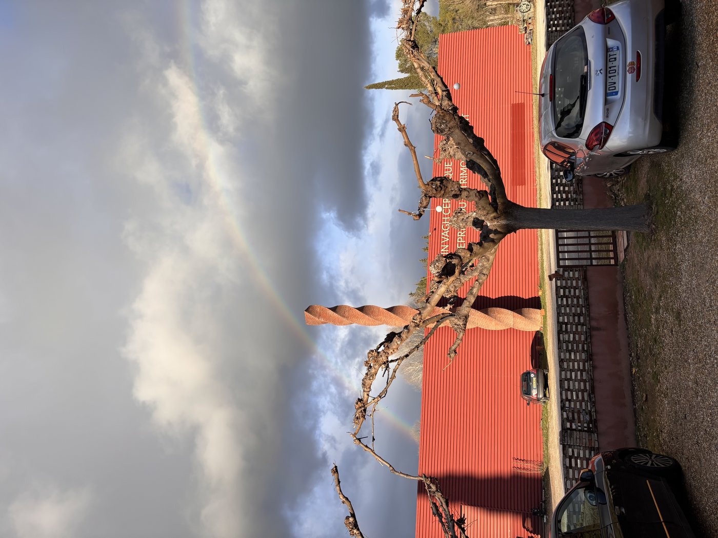 Façade de l'atelier sous un arc-en-ciel, avec la sculpture torsadée