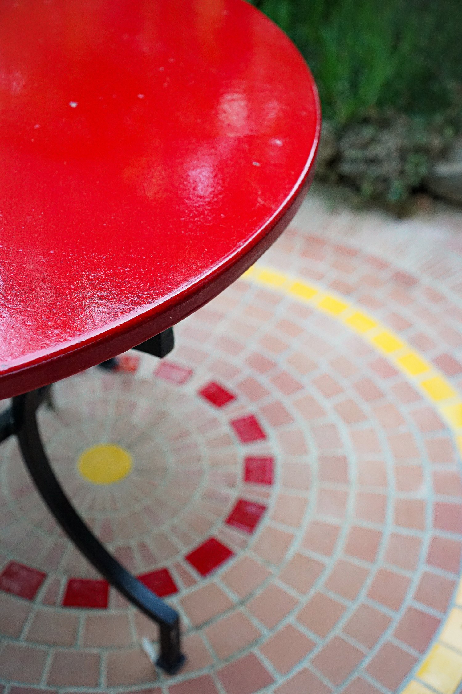 Gros plan sur une table ronde en lave émaillée rouge, posée sur une mosaïque de tomettes